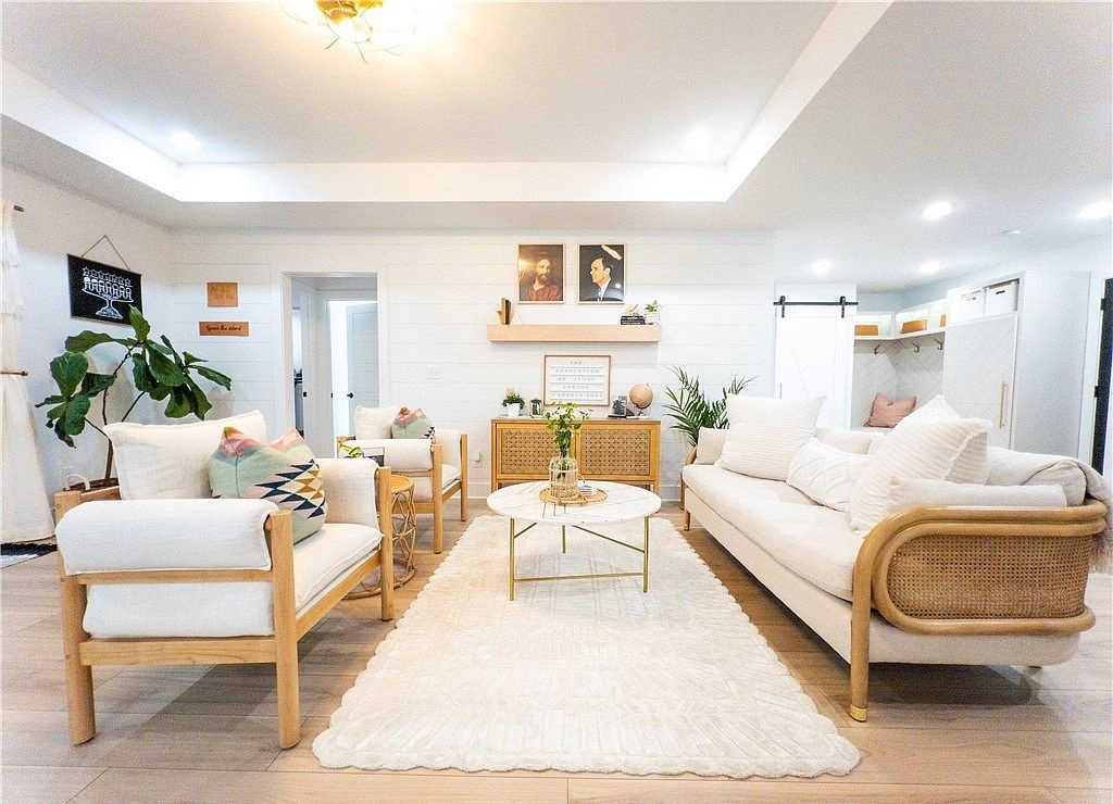 Furnished living room with cream seating, a white rug, plants, and a tray ceiling.