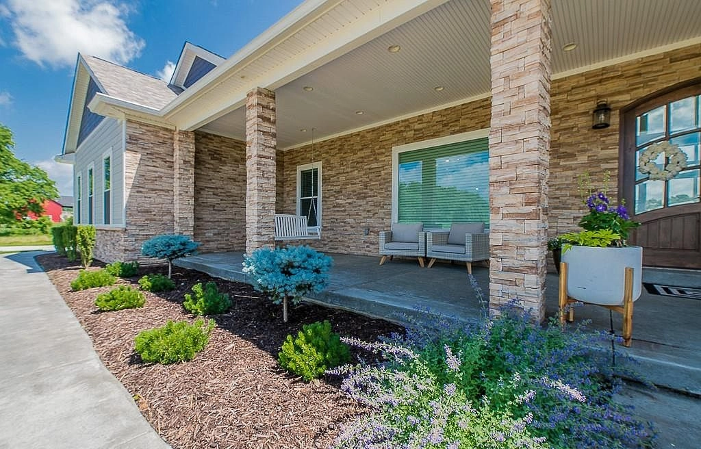 Stone porch columns beside planting beds and a broad front window