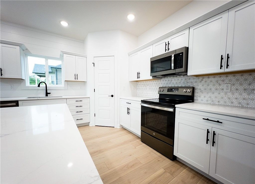 White kitchen cabinetry with black hardware, a patterned backsplash, range, and microwave.
