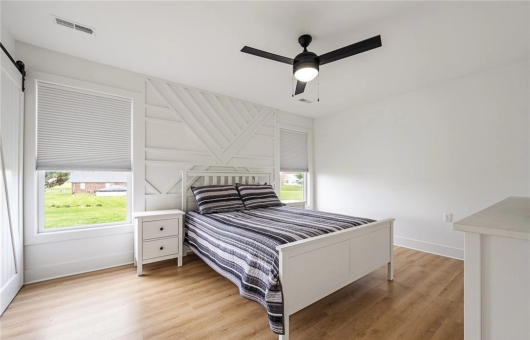 Bedroom with a paneled accent wall, ceiling fan and windows beside the bed