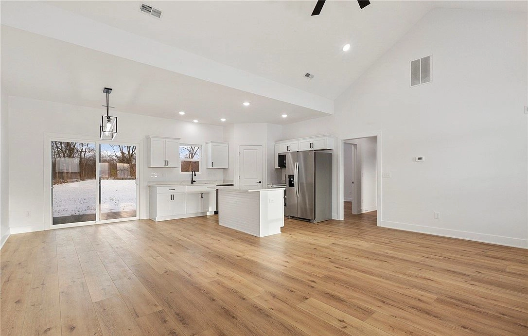 Open living area with wood-toned flooring, a high ceiling and a white kitchen