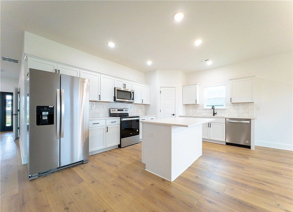 White kitchen with stainless steel appliances, a central island, and wood flooring.