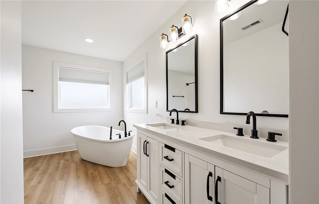 Bathroom with a white double vanity, dark fixtures and freestanding tub