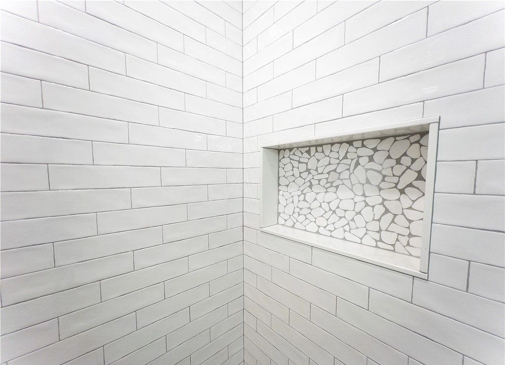 Rectangular shower niche with pale stone mosaic backing set into white subway tile.
