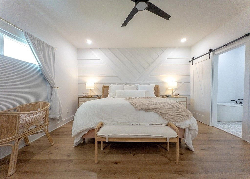 Bed and upholstered bench beneath a geometric accent wall beside a sliding bathroom door.