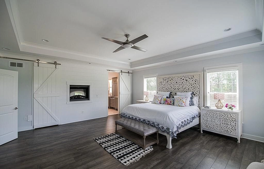 Bedroom with a tray ceiling and sliding bathroom doors beside a wall-mounted fireplace